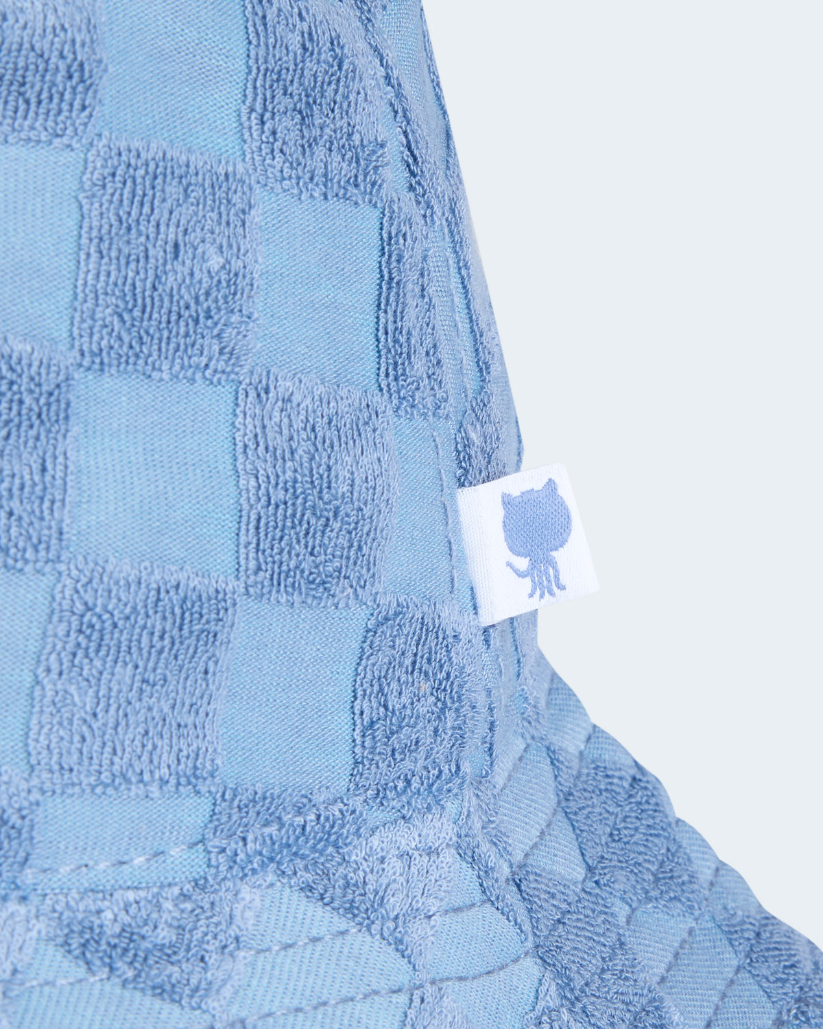 Close-up view of blue checkered bucket hat featuring the white label with Octocat logo attached on the side