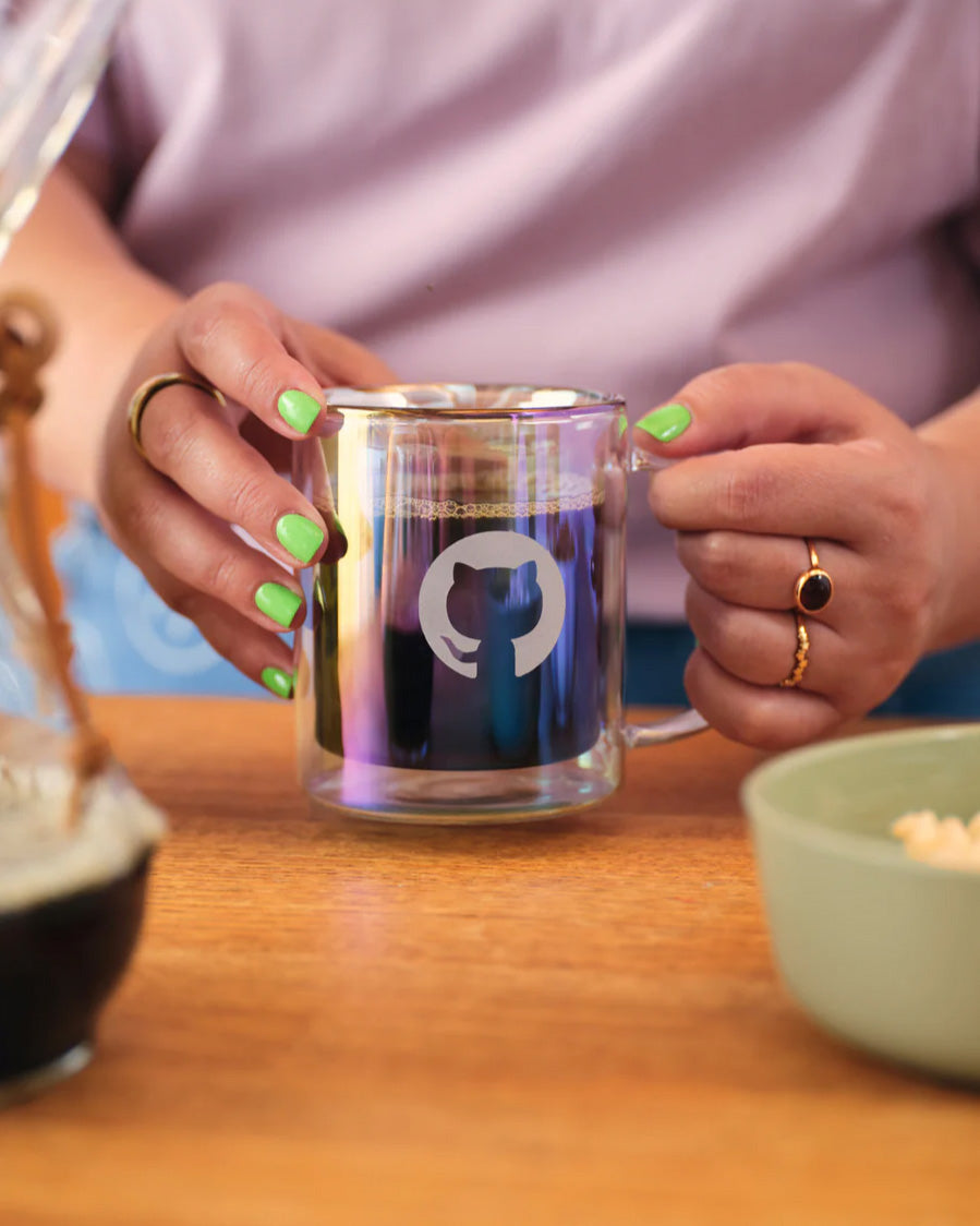 Person holding a glass mug with a logo on a wooden table