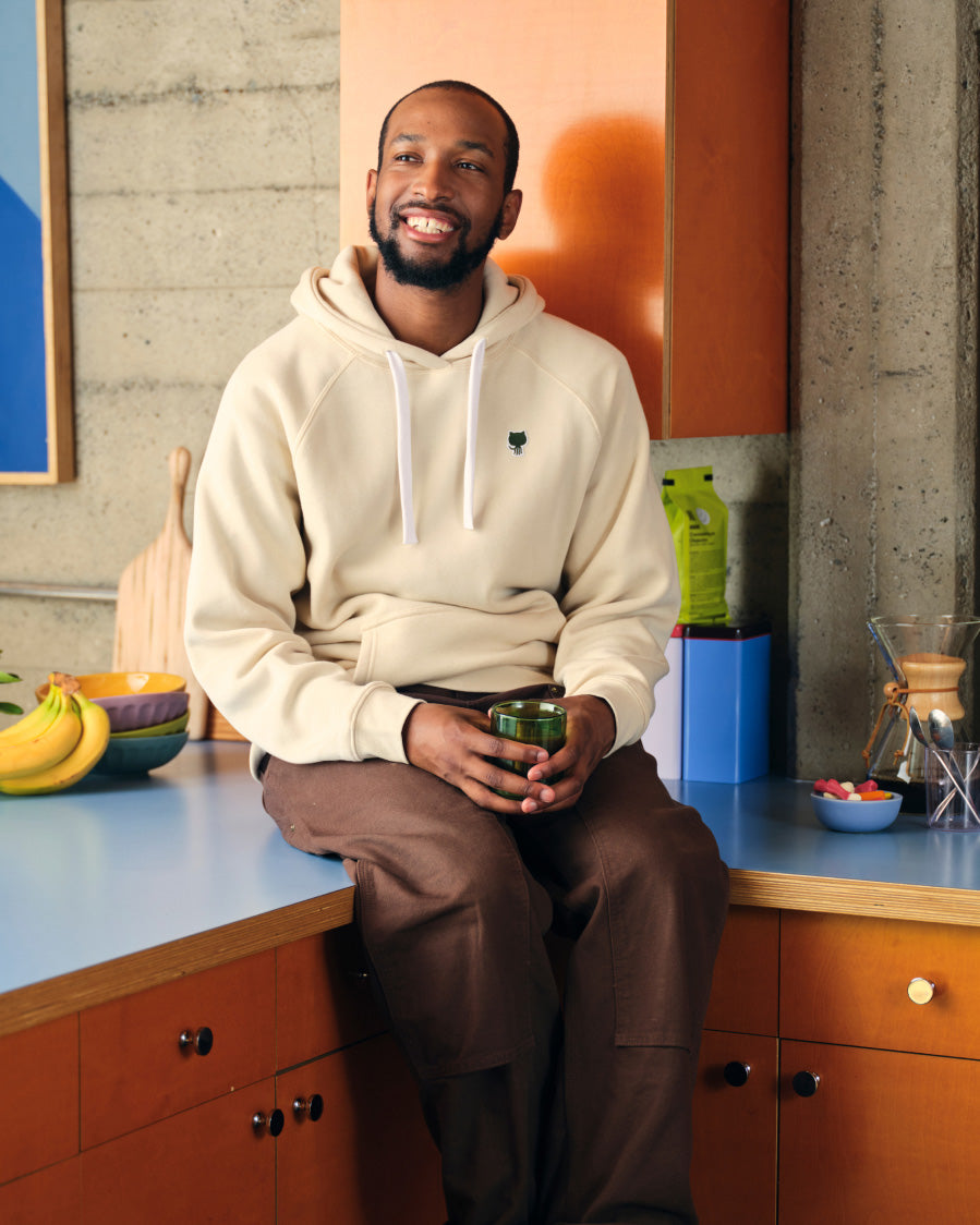 Man sitting at a kitchen counter wearing a GitHub  hoodie and brown pants.
