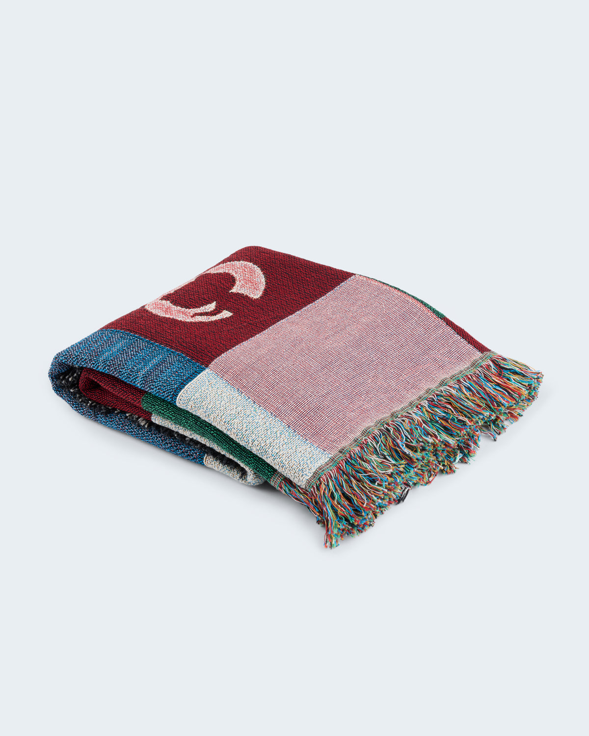 Folded woven throw blanket with multicolor patchwork design and fringe trim.