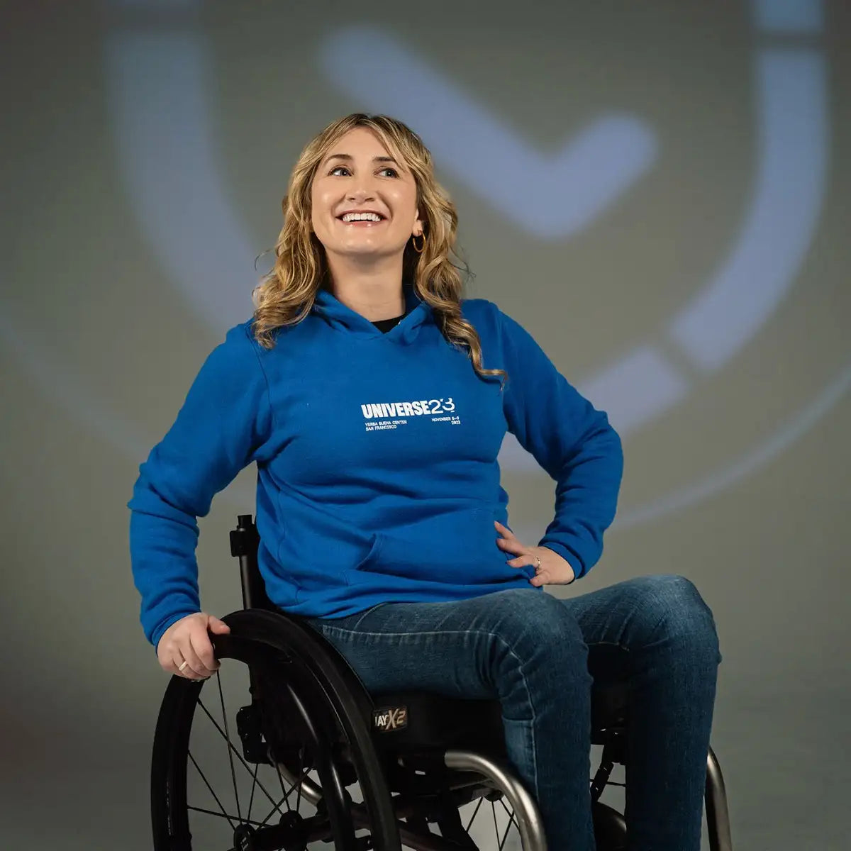 Photo of woman with blonde hair in a wheelchair wearing the blue Universe 2023 hoodie