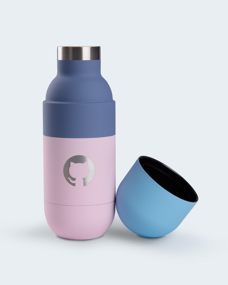 Pink and navy GitHub tumbler with stainless steel top, featuring a metallic Octocat logo at the center, shown with its pastel blue cup-style lid removed and placed beside it.