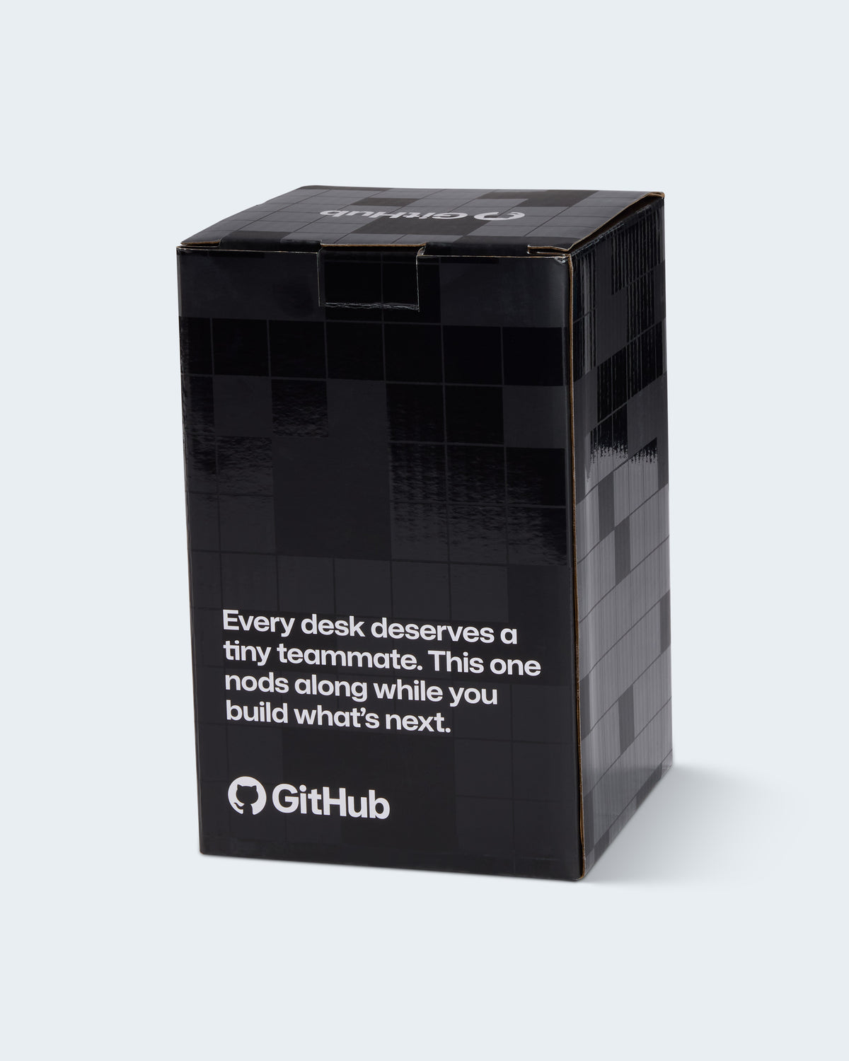 A black rectangular product box with white text reading 'Every desk deserves a tiny teammate. This one nods along while you build what's next.