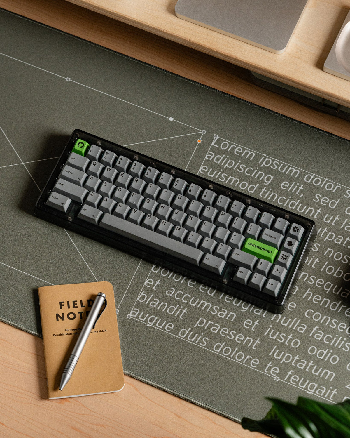 Compact mechanical keyboard on a desk mat beside a notebook and pen on a wooden desk.